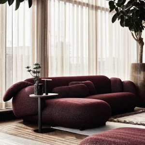 Moderne Leolux Pulla design hoekbank met ronde vormen en een chaise longue, uitgevoerd in bordeauxrode bouclé stof. Deze modulaire organische bank staat in een licht interieur met een visgraatvloer en kamerhoge gordijnen.