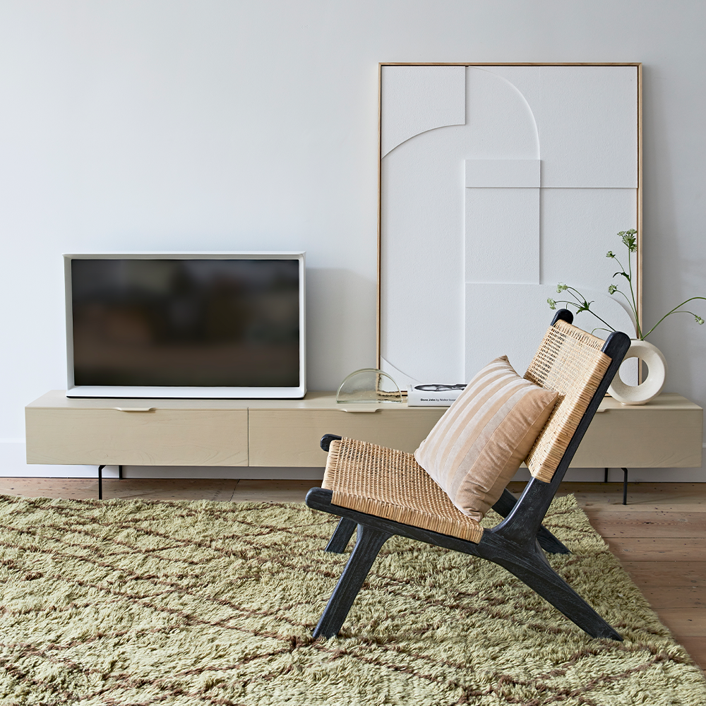 Tv meubel houtnerf 250 cm van HKliving in zandkleur met twee lades en een klep met een fauteuil, accessoires en een groene vloerkleed